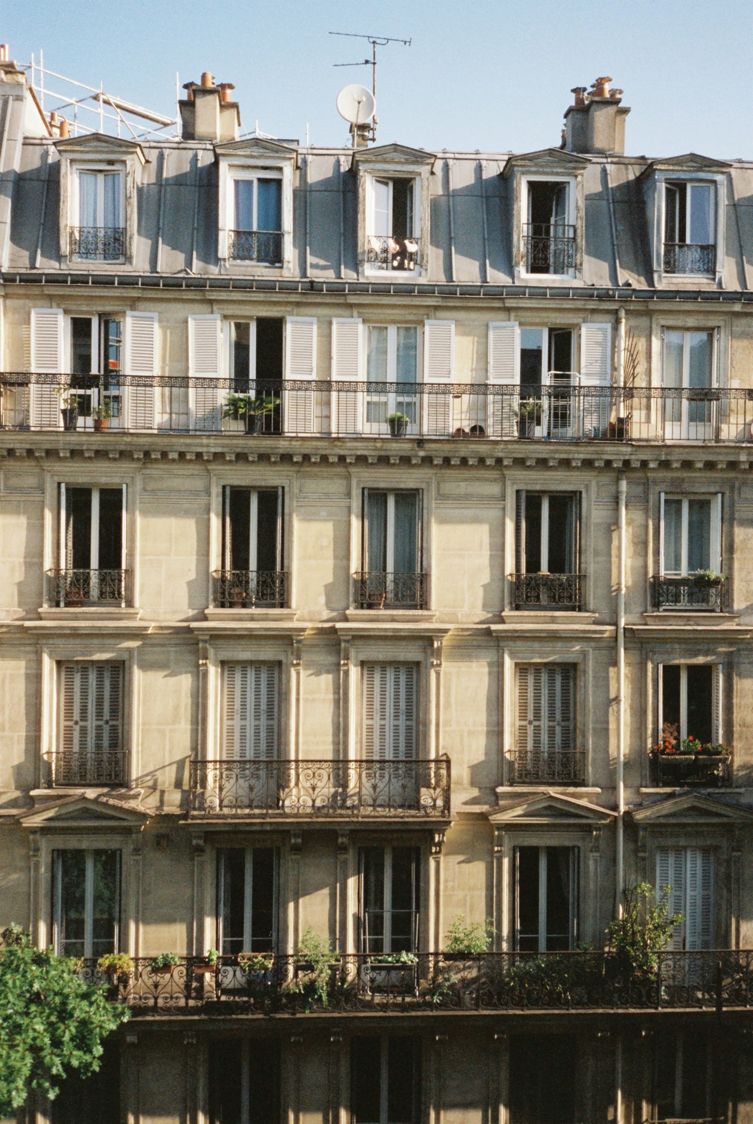 Façade d'un immeuble résidentiel ancien, fenêtres à volets, balcons filants et antenne sur le toit.